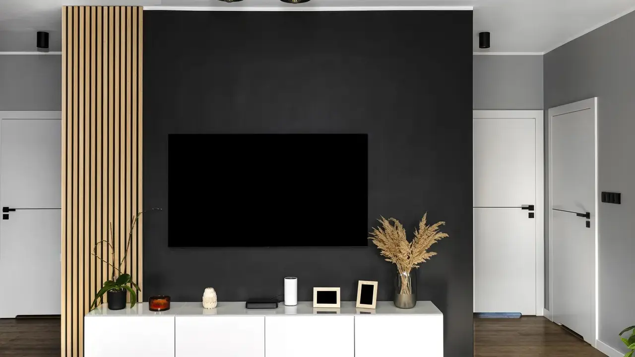Nowoczesny salon z czarną ścianą TV, białym meblem i drewnianą okładziną.