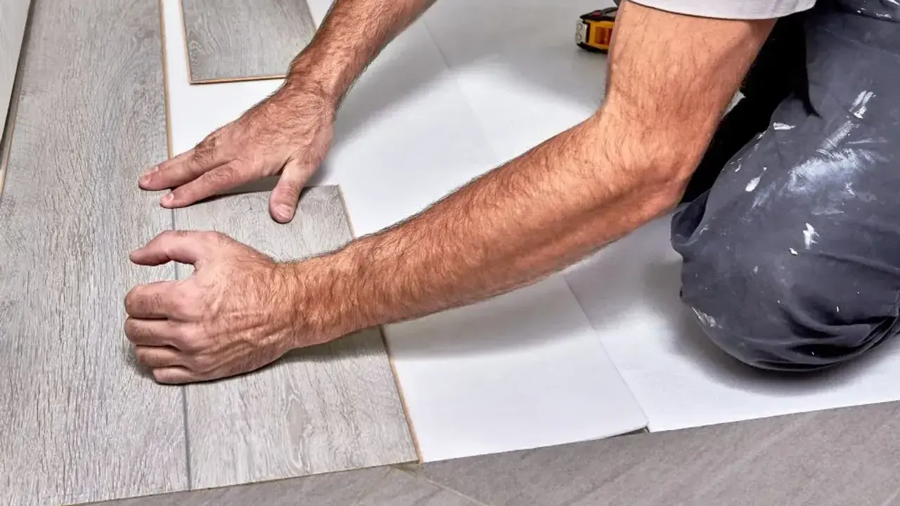 Ręce układają szare panele winylowe na białym podkładzie.