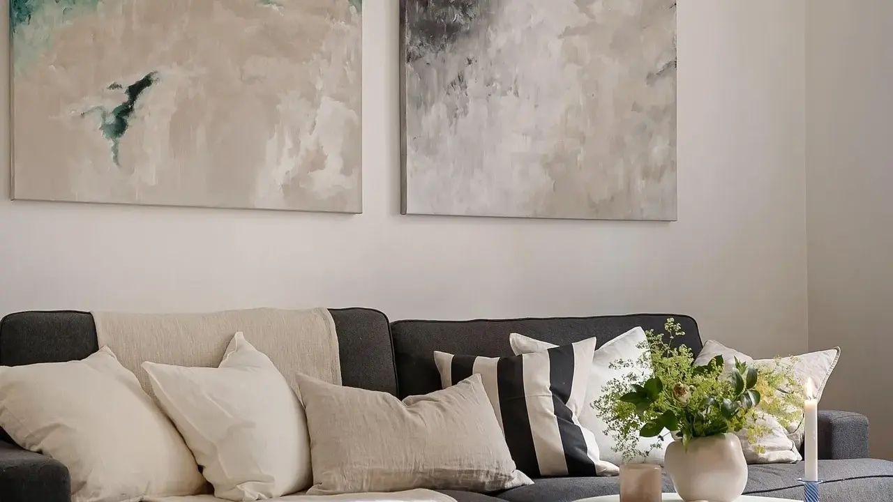 Sofa z poduszkami w neutralnych barwach i abstrakcyjne obrazy nad nią pokazują, jak łączyć kolory w stonowany sposób.