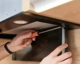 Ręce majsterkowicza przykręcają filtr w okapie bez wyciągu. Montaż okapu kuchennego.