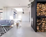 Nowoczesny salon z szarą sofą, czarno-białym dywanem i minimalistycznym **betonem na podłogę**. Obok kominek z drewnem.