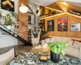 Przytulny mały pokój w stylu loft z ceglaną ścianą, metalowymi schodami, wiszącym fotelem i wygodną kanapą.