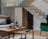 Nowoczesna zabudowa pod schodami z miejscem na wino i schowkami. Wygodny salon z szarą kanapą i zielonym fotelem.