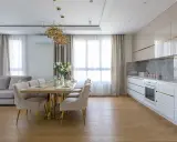 Elegancka kuchnia w stylu modern classic z jadalnią. Jasne meble, złote detale i wygodna sofa tworzą przytulną atmosferę.