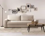 Beżowa kanapa z poduszkami i galerią ścienną z czarno-białych grafik. Aranżacje wnętrz z jasnym dywanem i stolikiem kawowym.