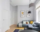 Nowoczesny salon z niebieską kanapą, dywanem i obrazami. Obok okna widać grzejnik, który można estetycznie zabudować.