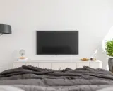 Nowoczesna sypialnia z dużym telewizorem na ścianie, wygodnym łóżkiem i stylową lampą.