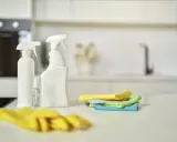 Gotowe do porządki w domu: żółte rękawice, butelki z płynem i kolorowe ściereczki z mikrofibry leżą na blacie kuchennym.