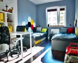 Nowoczesny pokój dla dwóch chłopców z dwoma łóżkami, biurkiem i regałem. Ściany zdobią kolorowe heksagony.