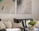 Sofa z poduszkami w neutralnych barwach i abstrakcyjne obrazy nad nią pokazują, jak łączyć kolory w stonowany sposób.