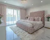 Elegancka, nowoczesna sypialnia glamour w odcieniach różu. Miękkie, pikowane łóżko, puszysty dywan i kryształowy żyrandol tworzą luksusową atmosferę.