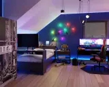 Nowoczesny pokój gamingowy na poddaszu z łóżkiem, biurkiem z potrójnym monitorem i kolorowym oświetleniem LED.