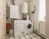 Małe pomieszczenie gospodarcze w domu z pralką, suszarką, bojlerem i szafą.