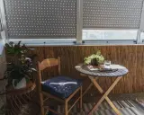 Przytulna loggia: drewniane krzesło z poduszką, stolik z wodą i roślinami, bambusowa ściana. Idealne miejsce na relaks.