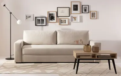Beżowa kanapa z poduszkami i galerią ścienną z czarno-białych grafik. Aranżacje wnętrz z jasnym dywanem i stolikiem kawowym.