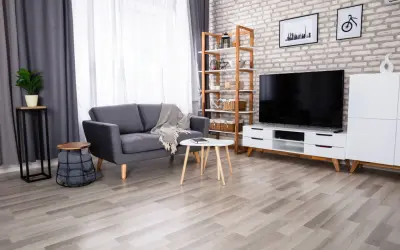 Nowoczesna aranżacja salonu z szarą podłogą, szarą kanapą, białym stolikiem i regałem z dekoracjami.