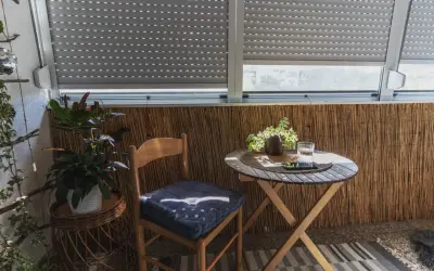 Przytulna loggia: drewniane krzesło z poduszką, stolik z wodą i roślinami, bambusowa ściana. Idealne miejsce na relaks.