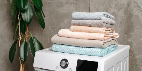Stos czystych ręczników na pralce. Zastanawiasz się, w jakiej temperaturze prać ręczniki, by były świeże i miękkie?