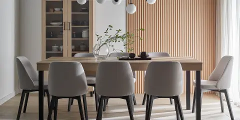 Nowoczesna jadalnia z drewnianym stołem i szarymi krzesłami. Wisząca lampa znajduje się na odpowiedniej wysokości nad stołem, tworząc przytulną atmosferę.