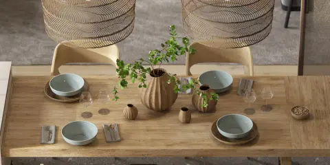 Drewniany stół w jadalni w stylu boho, nakryty do posiłku. Wazon z gałązkami i liśćmi, misy, kieliszki i plecione lampy tworzą przytulną atmosferę.
