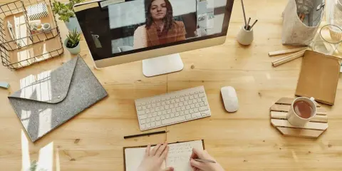 Uporządkowane biurko w pracy: komputer z wideokonferencją, notatnik, kubek z herbatą i akcesoria.