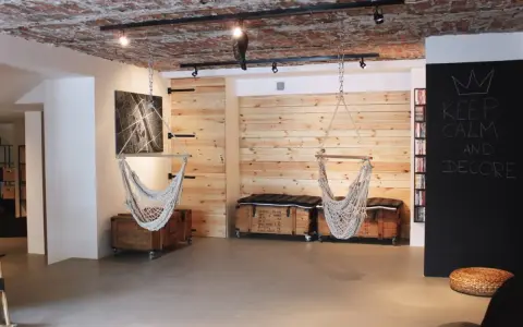 Nowoczesna aranżacja piwnicy w domu: wiszące fotele, drewniane panele, skrzynie i tablica z napisem "Keep Calm and Decore".