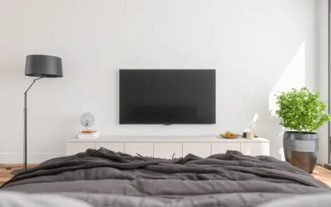 Nowoczesna sypialnia z dużym telewizorem na ścianie, wygodnym łóżkiem i stylową lampą.