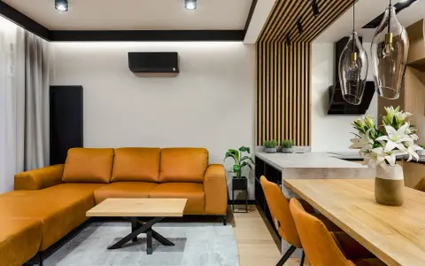 Nowoczesne wnętrze z pomarańczową kanapą i stołem. Widoczne mocowanie lameli do sufitu, tworzące ciekawy detal architektoniczny.
