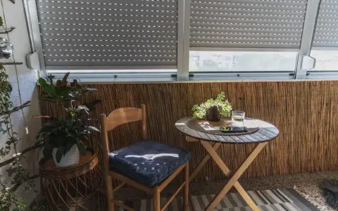 Przytulna loggia: drewniane krzesło z poduszką, stolik z wodą i roślinami, bambusowa ściana. Idealne miejsce na relaks.