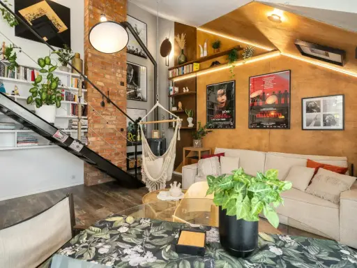 Przytulny mały pokój w stylu loft z ceglaną ścianą, metalowymi schodami, wiszącym fotelem i wygodną kanapą.