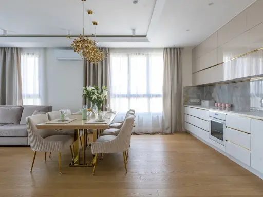 Elegancka kuchnia w stylu modern classic z jadalnią. Jasne meble, złote detale i wygodna sofa tworzą przytulną atmosferę.