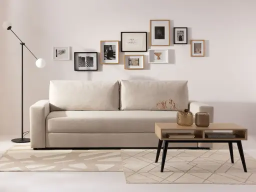Beżowa kanapa z poduszkami i galerią ścienną z czarno-białych grafik. Aranżacje wnętrz z jasnym dywanem i stolikiem kawowym.