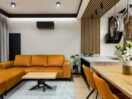 Nowoczesne wnętrze z pomarańczową kanapą i stołem. Widoczne mocowanie lameli do sufitu, tworzące ciekawy detal architektoniczny.