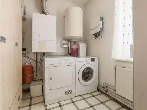 Małe pomieszczenie gospodarcze w domu z pralką, suszarką, bojlerem i szafą.
