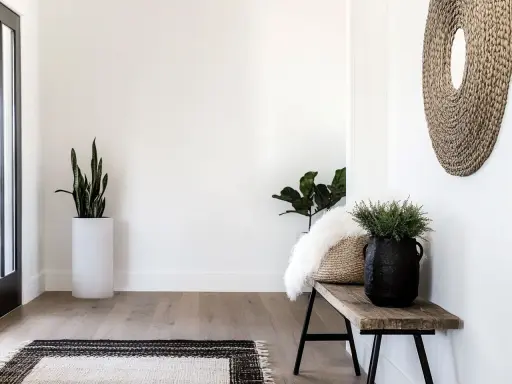 Przytulny przedpokój w stylu boho z drewnianą ławką, plecionym lustrem i roślinami.