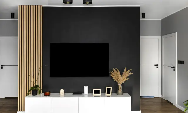Nowoczesny salon z czarną ścianą TV, białym meblem i drewnianą okładziną.