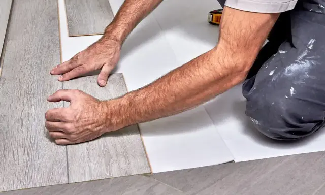 Ręce układają szare panele winylowe na białym podkładzie.