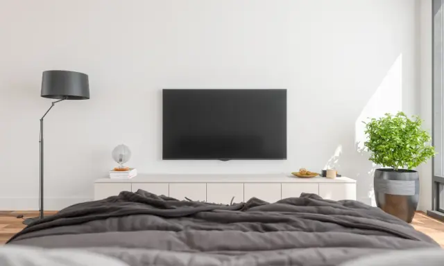 Nowoczesna sypialnia z dużym telewizorem na ścianie, wygodnym łóżkiem i stylową lampą.