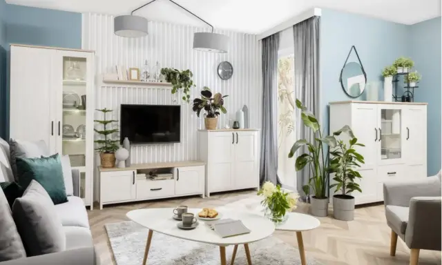 Nowoczesny salon z białymi meblami i dużą ilością zielonych kwiatów.