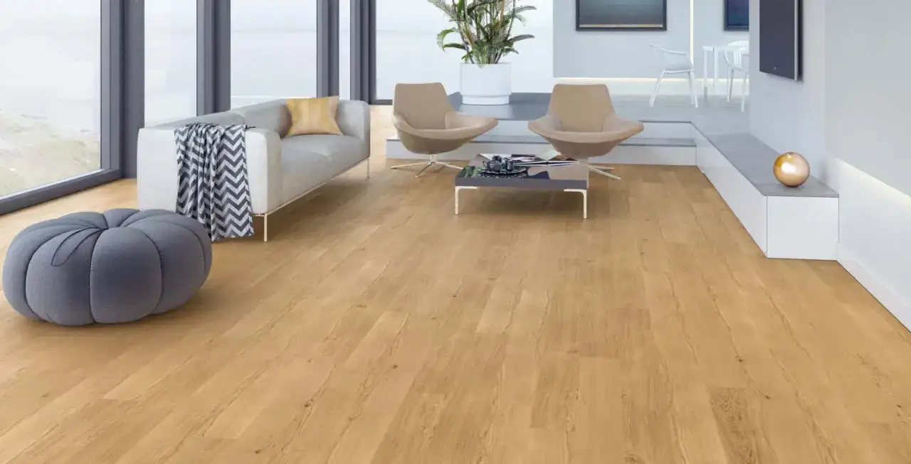 Nowoczesny salon z drewnianą podłogą. Szara pufa i kanapa świetnie komponują się z ciepłym odcieniem drewna, tworząc przytulną atmosferę. Kolor taupe z czym łączyć? Z naturalnymi barwami i szarościami.
