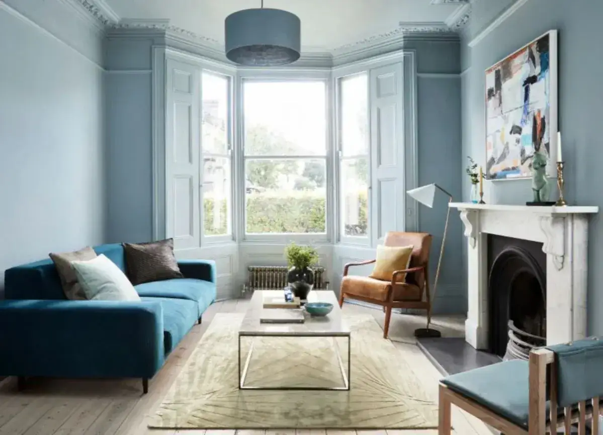 Elegancki salon z sofą w kolorze petrol blue, skórzanym fotelem i kominkiem.