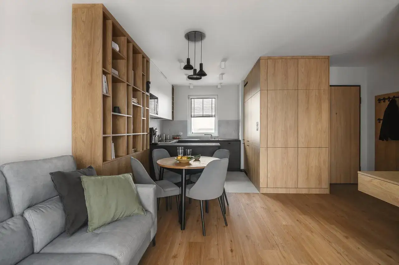 Nowoczesne oświetlenie salonu z jadalnią aranżacje: designerskie lampy nad okrągłym stołem, drewniane regały i szafy tworzą przytulną atmosferę.