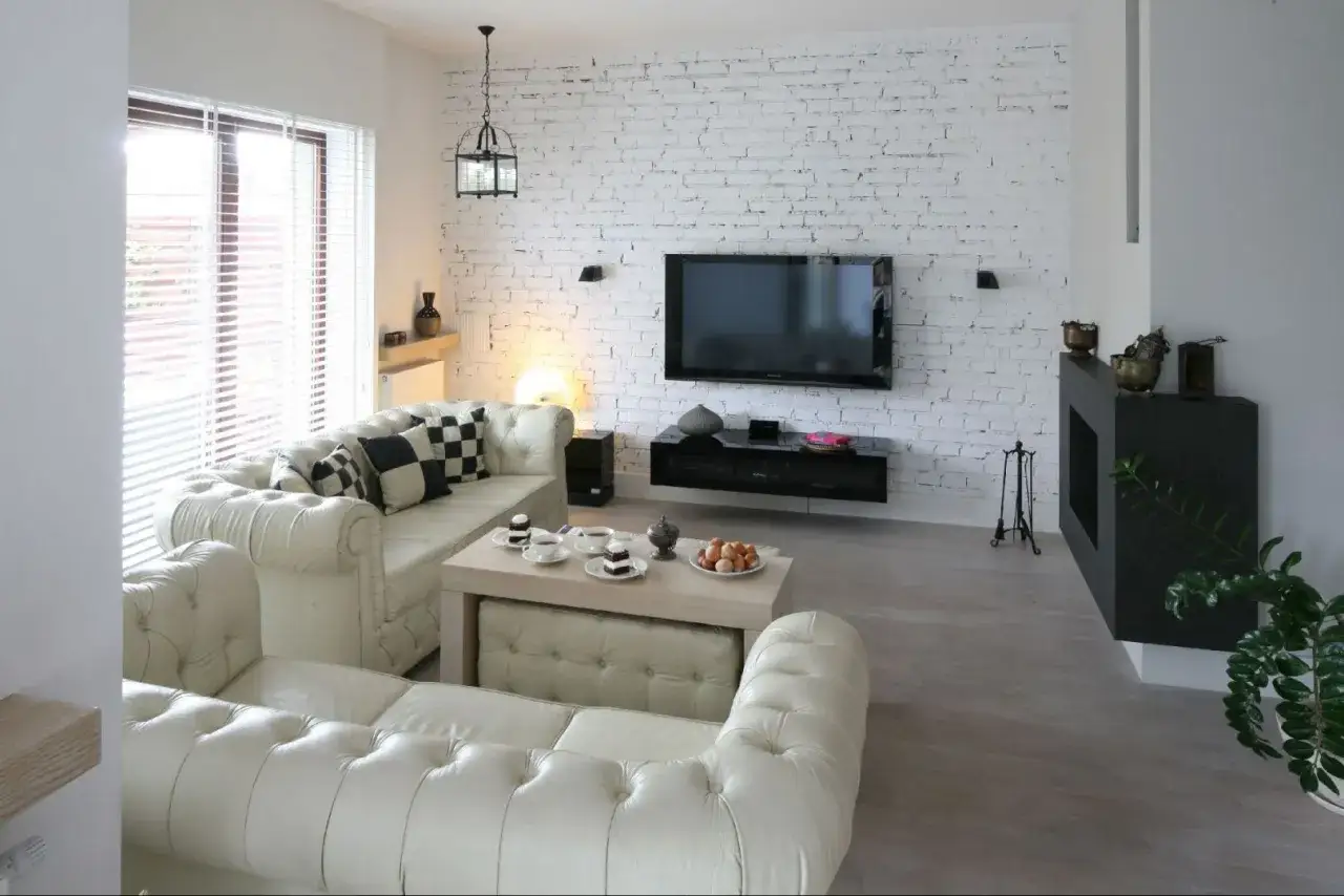 Nowoczesny salon z sofami w stylu chesterfield i ścianą z białej cegły, która stanowi centralny punkt aranżacji.