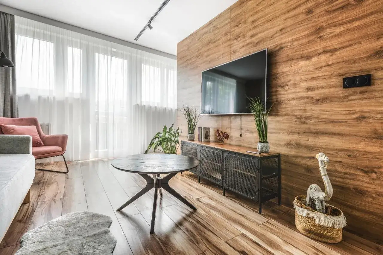 Mały pokój inspiracje: przytulna kanapa, różowy fotel, okrągły stolik i drewniana ściana z TV.