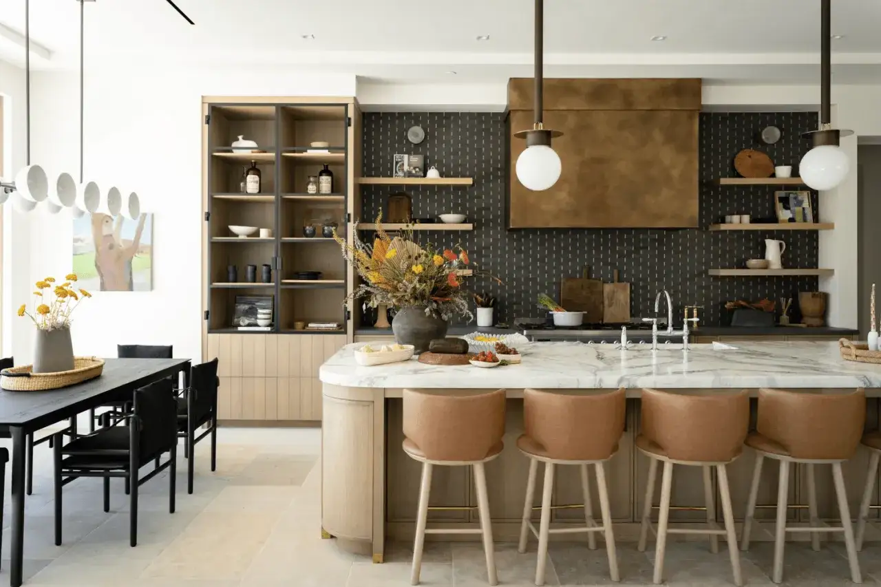 Nowoczesna kuchnia z wyspą, gdzie dominują naturalne materiały. Ciepłe drewno w zabudowie i meblach tworzy przytulną atmosferę, a marmurowy blat dodaje elegancji. Kuchnia inspiracje czerpie z natury.