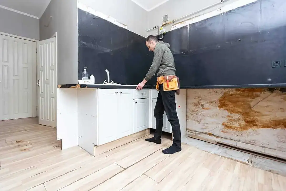 Remont kuchni od czego zacząć? Mężczyzna w pasie narzędziowym ogląda szafki kuchenne.