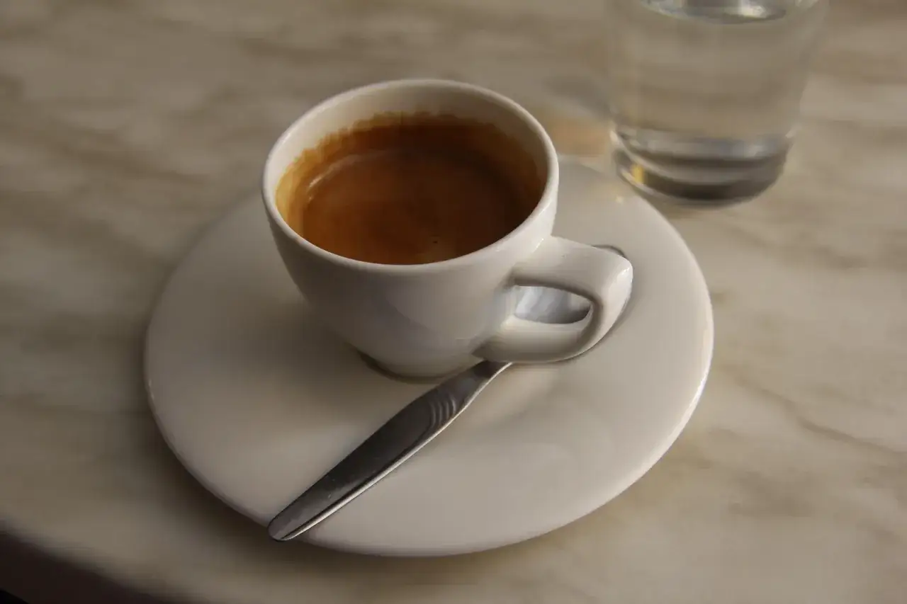 Elegancka filiżanka kawy espresso na talerzyku z łyżeczką i szklanką wody. Idealny sposób, jak podawać kawę gościom, by poczuli się wyjątkowo.