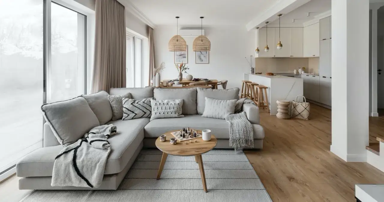 Przytulny salon z szarą sofą, drewnianym stolikiem i szachami. Naturalne materiały i jasne kolory pomagają ocieplić wnętrze.