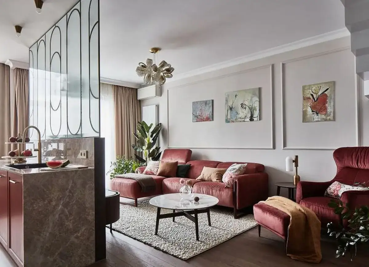 Nowoczesny salon z czerwoną kanapą i fotelami. Na ścianie wiszą trzy obrazy, które dodają koloru i charakteru.