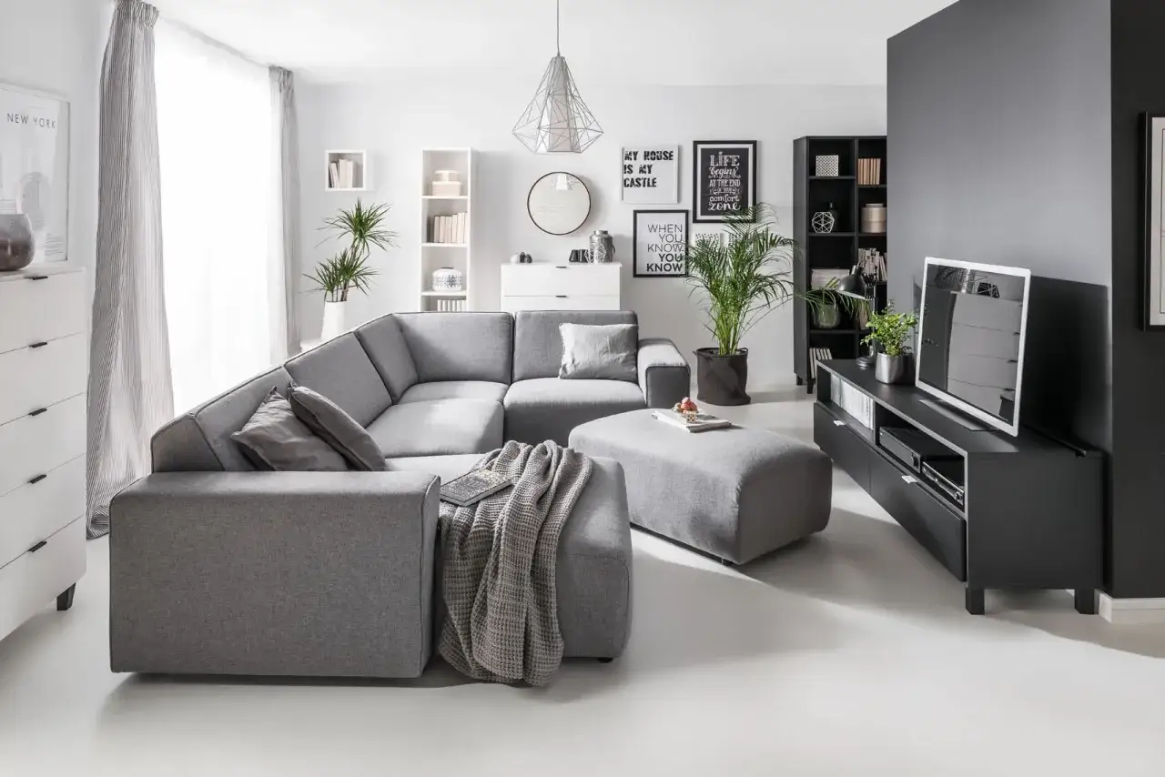 Szary salon z wygodną sofą i pufą, inspiracja, jak ocieplić szary salon. Dodatki i rośliny nadają przytulności.